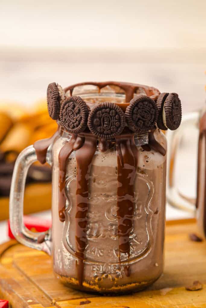 A mason jar of Chocolate Freakshake with chocolate drips and mini chocolate sandwich cookies on the rim.