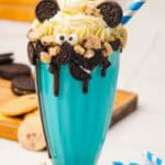 Blue Cookie Monster milkshake topped with whipped cream, mini cookies, chocolate, and candy eyes, served with a blue-striped straw—an irresistible Cookie Monster dessert!.