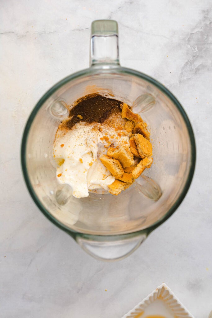 Top view of a blender containing cream, spices, and crumbled cookies&mdash;perfect for crafting a festive Gingerbread Freakshake or adding a sweet twist to your favorite Christmas Recipe.