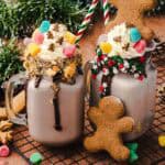 Two festive mugs of hot chocolate topped with whipped cream, candies, and gingerbread cookies on a cooling rack—perfect for a cozy Christmas Recipe or your next Gingerbread Freakshake craving.