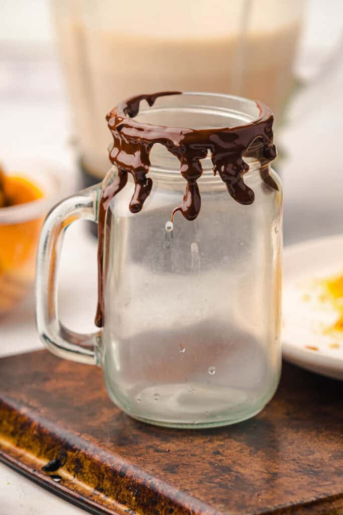 A glass jar mug with chocolate sauce dripped around the rim, sitting on a rustic tray&mdash;perfect for serving a Gingerbread Freakshake as a festive Christmas Recipe.