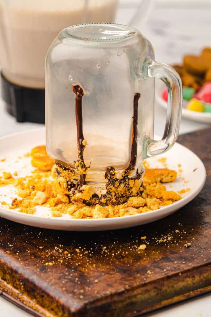 A mason jar turned upside down with chocolate and cookie crumbs on its rim, sitting on a white plate &ndash; perfect for serving a festive Gingerbread Freakshake or any creative Christmas Recipe.