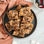 A plate of Rice Krispies treats topped with chocolate chunks and festive sprinkles on a marble surface.