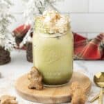 Iced Matcha Latte with whipped cream in a mason jar, topped with cinnamon and served alongside delicious gingerbread cookies.