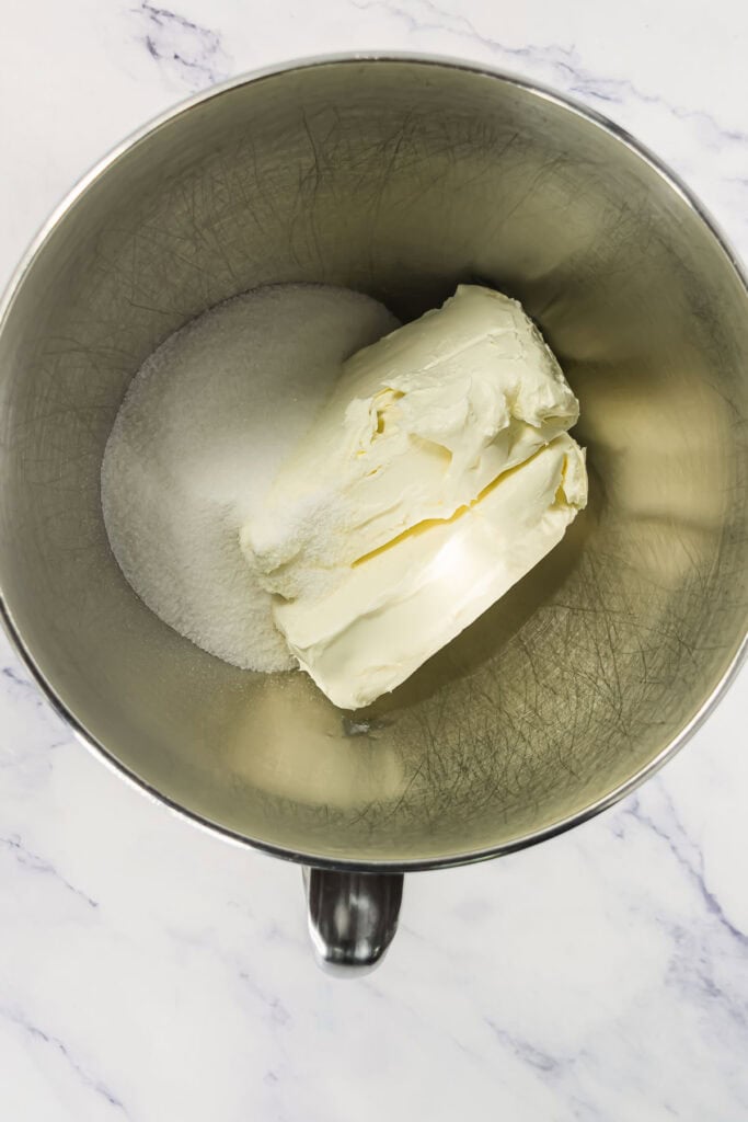 Butter and sugar in a metal mixing bowl on a marble countertop, ready to be mixed.