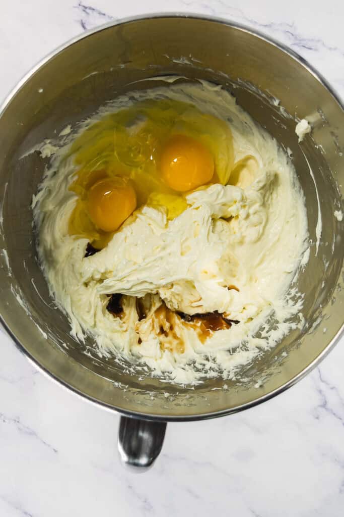 A mixing bowl with two eggs on top of creamy batter, ready to be mixed, on a marble surface.