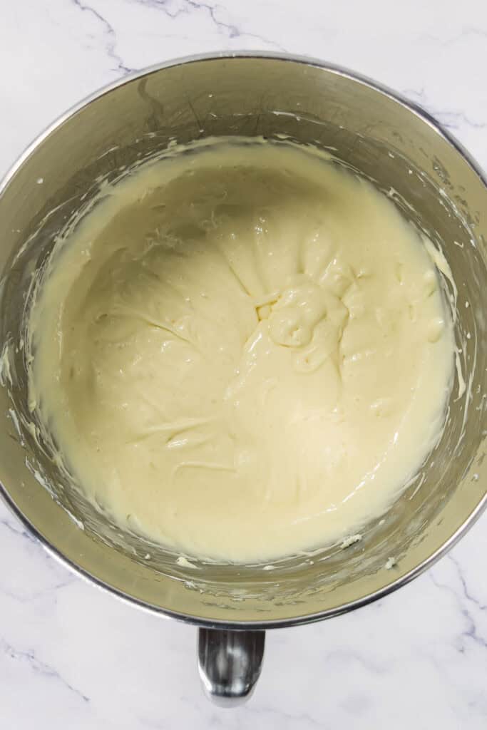 Thick, creamy cheesecake batter in a metal mixing bowl on a white marble surface.