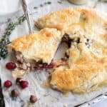 Rustic cranberry and hazelnut galette made with buttery puff pastry, a slice cut out, on parchment with scattered cranberries and nuts. Perfect as a cranberry brie appetizer for festive gatherings.