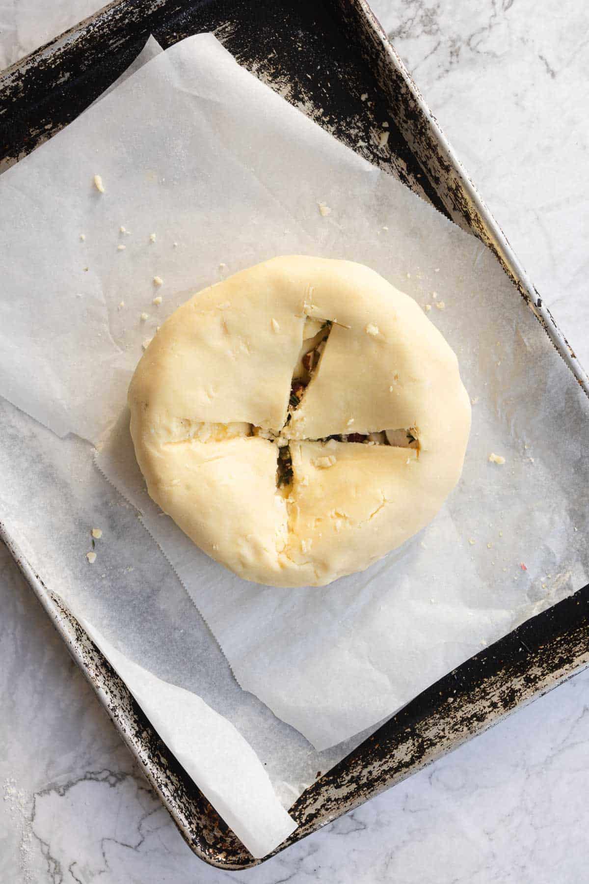 Unbaked round puff pastry with an X-shaped cut on top, perfect for making a cranberry brie appetizer, placed on parchment paper in a baking tray.