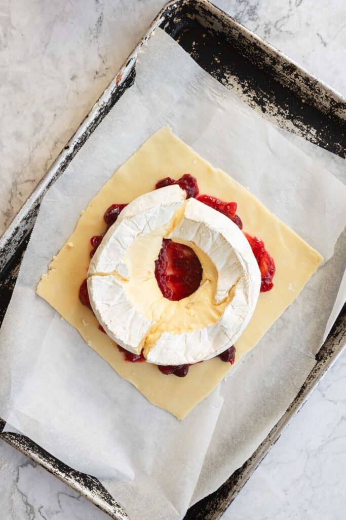 Square puff pastry topped with cranberry brie and a ring of jam, arranged on a parchment-lined baking sheet.