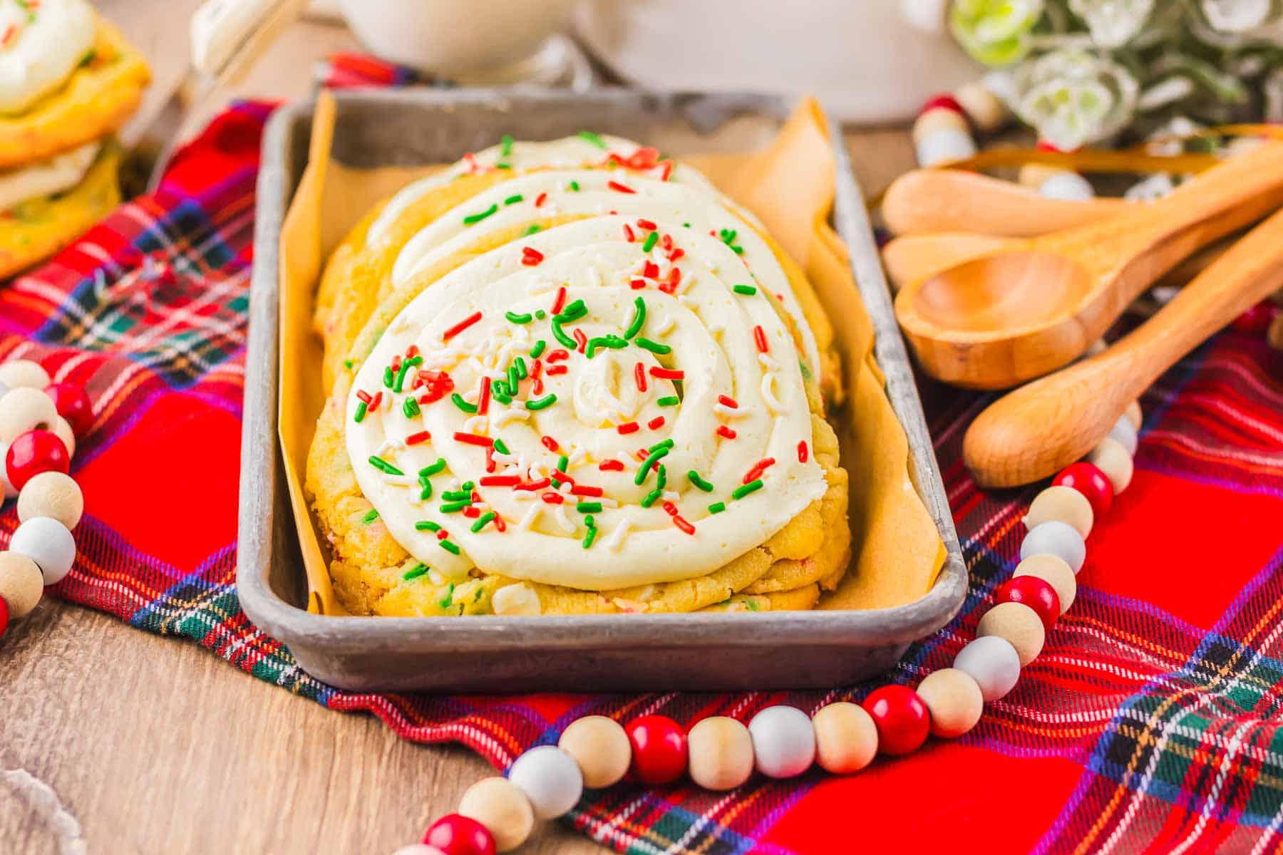Christmas cookies made from cake mix, frosted and topped with red and green sprinkles, arranged on a tray over a festive red plaid cloth with wooden beads.
