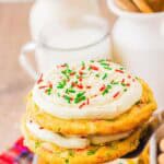 A frosted sugar cookie with red and green sprinkles is held above a tray of Christmas cookies, with milk in the background—an easy holiday treat made from cake mix.