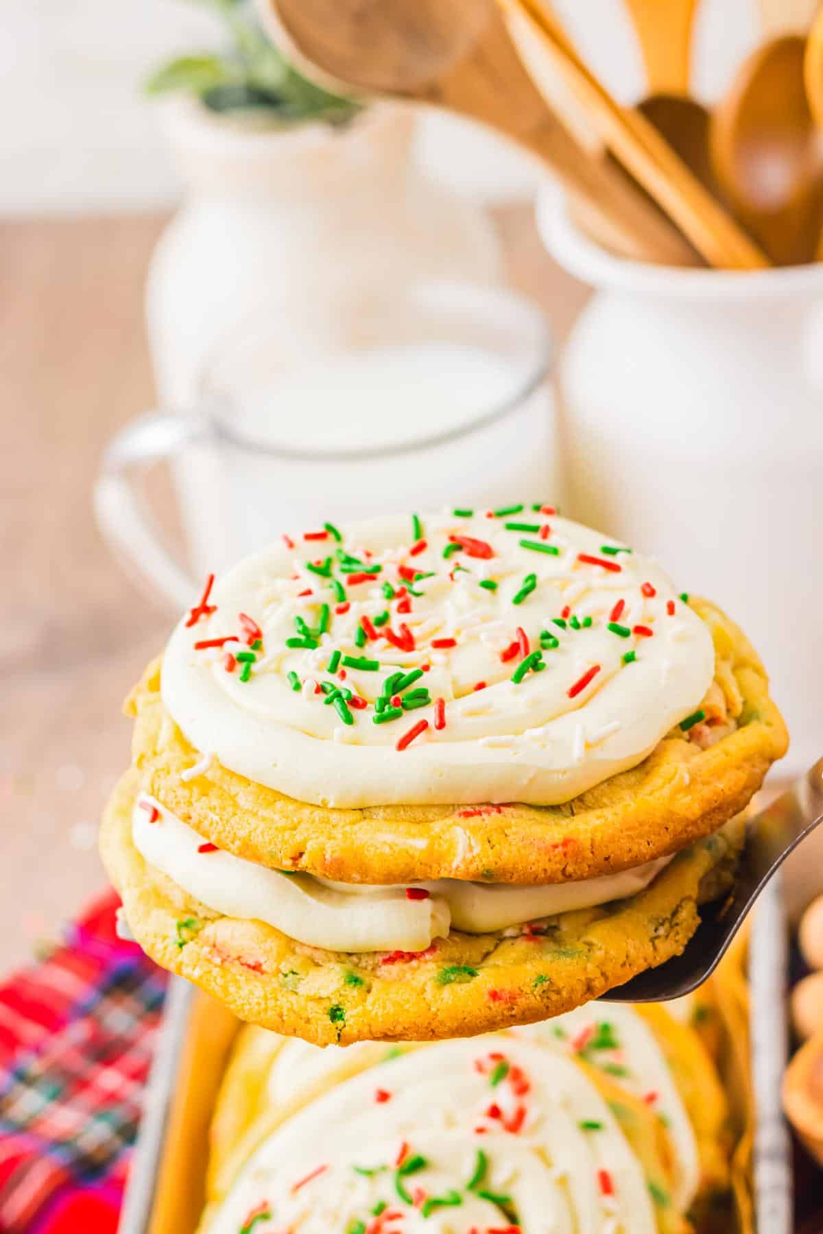 A frosted sugar cookie with red and green sprinkles is held above a tray of Christmas cookies, with milk in the background&mdash;an easy holiday treat made from cake mix.