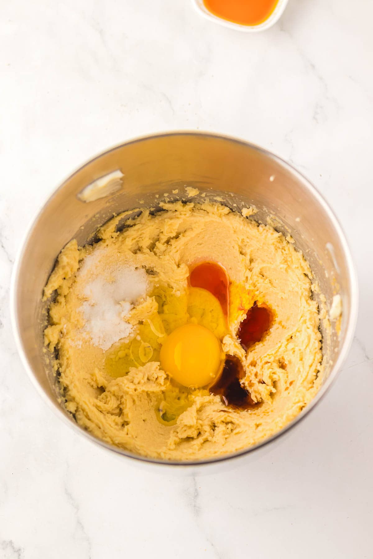 A mixing bowl with dough, an egg, vanilla extract, and cake mix among other ingredients on a white surface&mdash;perfect for starting a delicious recipe.