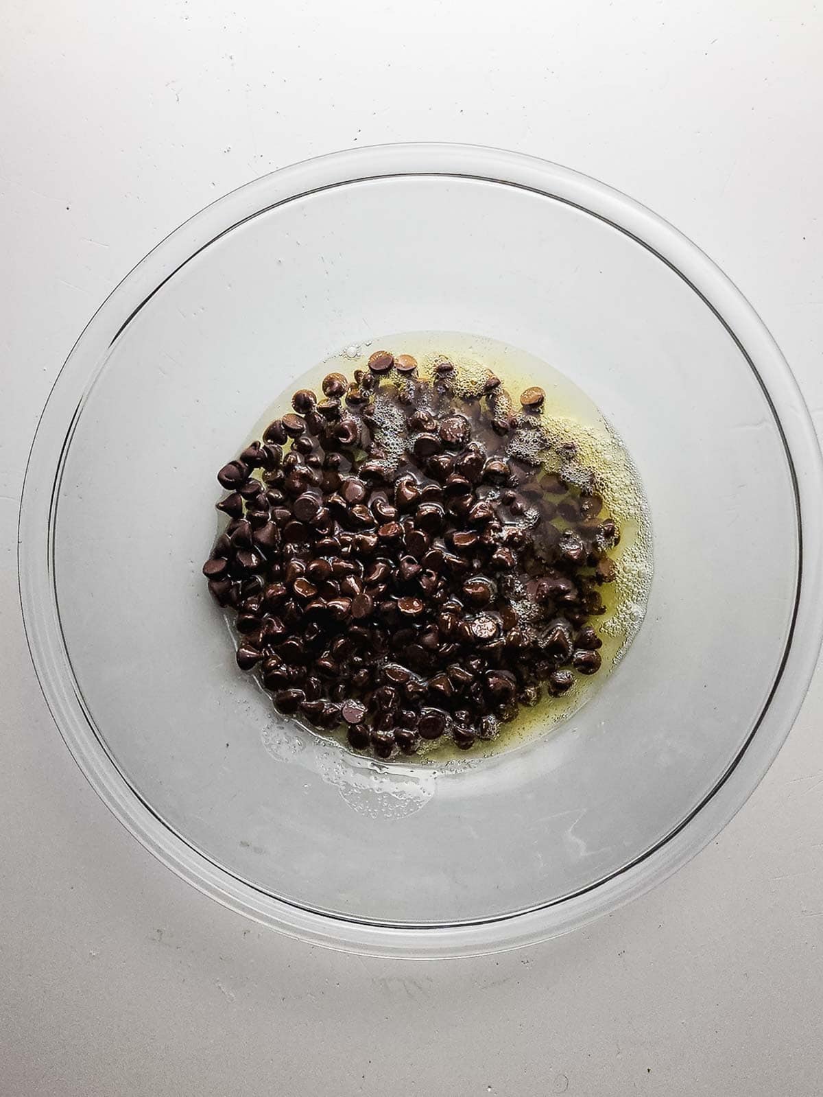 A glass bowl with melted butter and chocolate chips on a white surface, ready to be mixed for fudgy brownie cookies.
