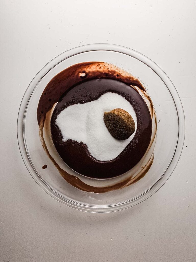 A glass bowl with cocoa powder, sugar, and a mound of brown sugar on a white surface&mdash;perfect beginnings for rich, fudgy brownie cookies.