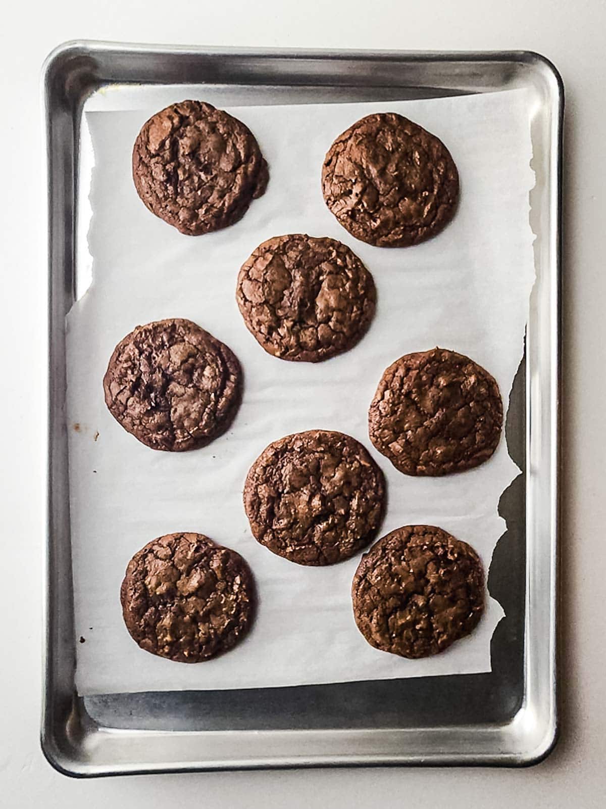 Eight fudgy brownie cookies on a parchment-lined baking sheet, viewed from above.