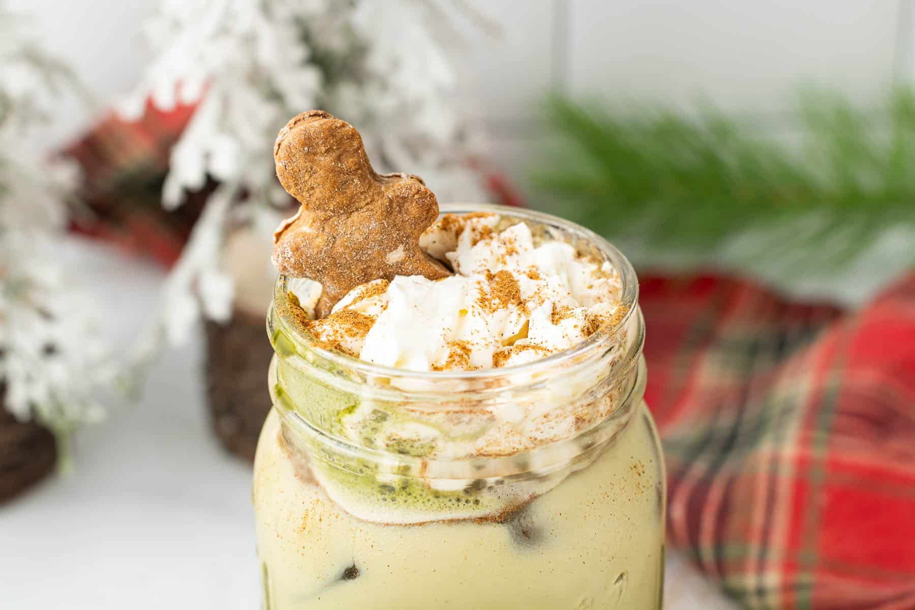 Iced Gingerbread Matcha Latte in a mason jar, topped with whipped cream, cinnamon, and a gingerbread cookie.