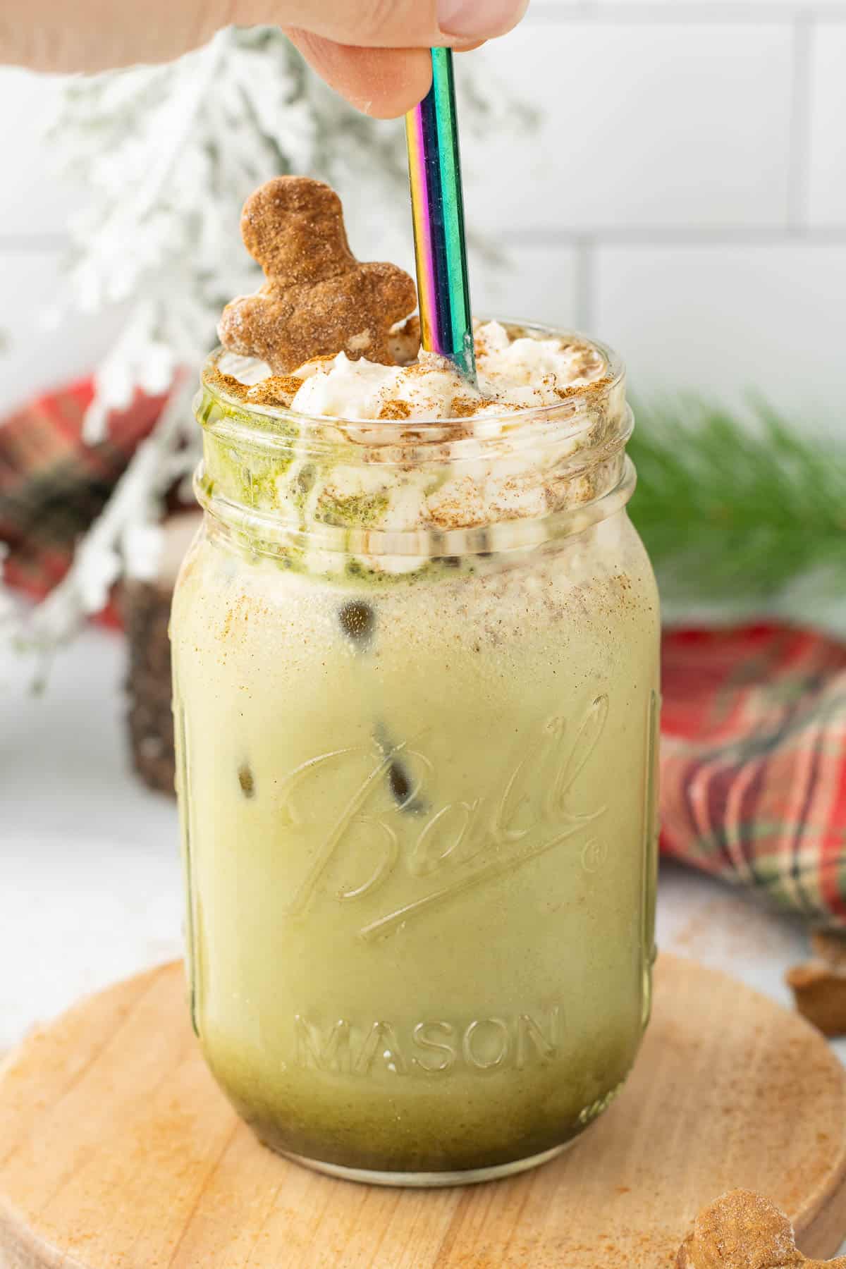 Iced Gingerbread Matcha Latte in a mason jar topped with whipped cream, cinnamon, and a gingerbread cookie.