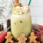 Iced Gingerbread Matcha Latte in a mason jar with whipped cream, topped with mini gingerbread cookies and a striped straw.