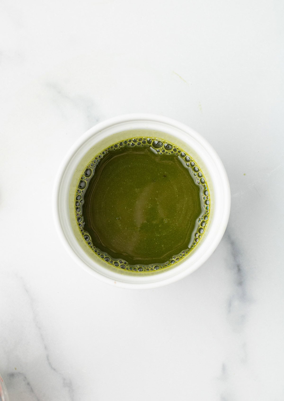 A white cup filled with a creamy gingerbread matcha latte sits on a white marble surface, viewed from above.