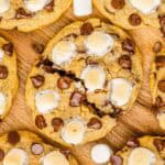 Top view of S'mores cookies with toasted marshmallows on a wooden surface, inspired by the classic s'mores recipe, with some mini marshmallows scattered nearby.