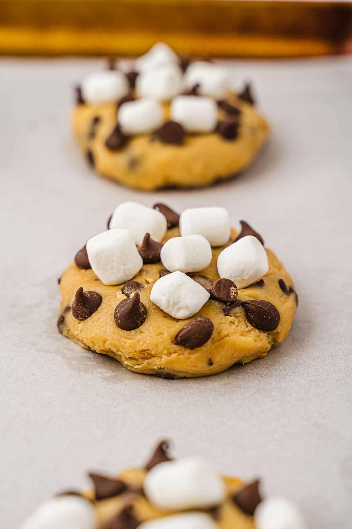 A close-up of a chocolate chip cookie topped with chocolate chips and mini marshmallows on parchment paper, perfect for any S'mores cookies lover or anyone searching for the ultimate cookies recipe.