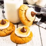 Three Blossom Cookies with toasted marshmallows and chocolate sit beside a glass of milk with straws and a bowl of marshmallows.