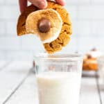 A hand dips a s'mores cookie with a bite missing into a glass of milk, bringing to mind the comforting taste of Peanut Butter Cookies.