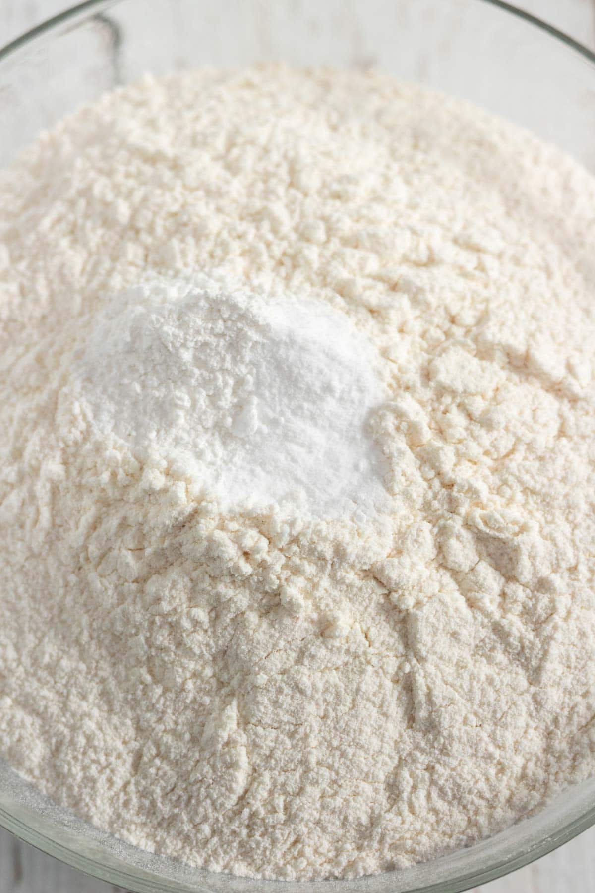 A glass bowl filled with flour and a mound of white baking powder on top, ready to be mixed into delicious Peanut Butter Cookies.