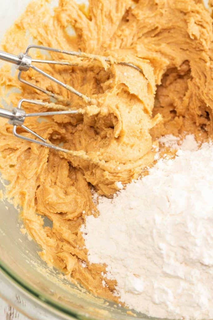 Electric mixer blending cookie dough with flour and creamy peanut butter in a glass bowl&mdash;perfect for making delicious Peanut Butter Cookies.