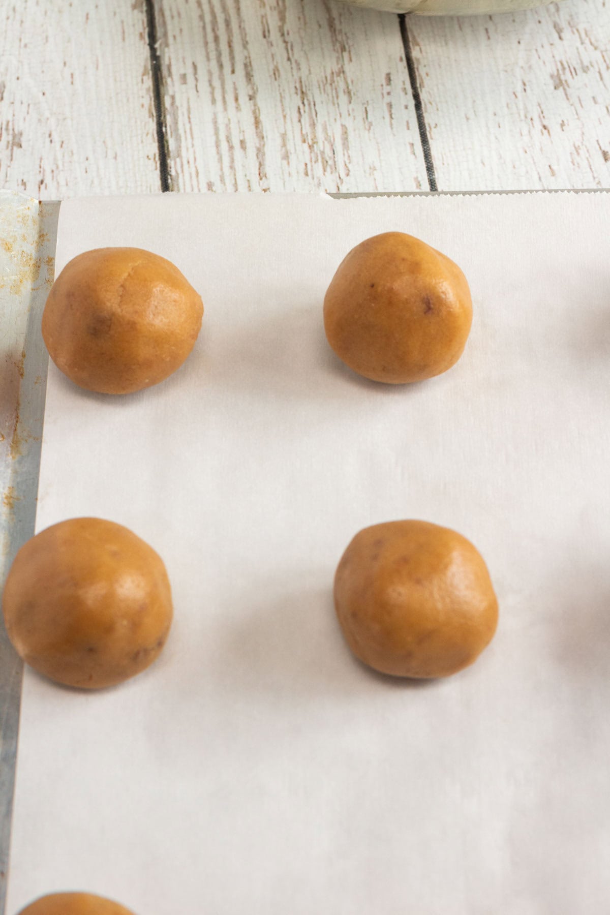Six round peanut butter cookie dough balls on parchment paper, ready for baking, on a white wooden surface&mdash;perfect for making classic blossom cookies.