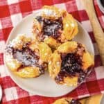 Three flaky pastry tarts filled with jam and dusted with powdered sugar on a white plate, reminiscent of a Starbucks Sugar Plum Cheese Danish copycat.