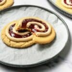 A crumbl copycat peanut butter and jelly cookie with swirled icing and jam, featuring a bite taken out, rests on a parchment-lined plate.
