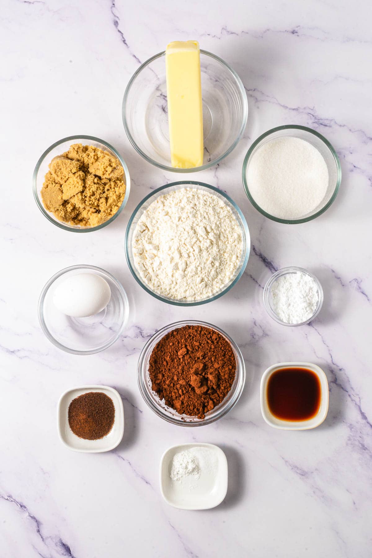 Baking ingredients for Chocolate Linzer Cookies include butter, brown sugar, sugar, flour, cocoa powder, egg, and small bowls of spices and liquids.