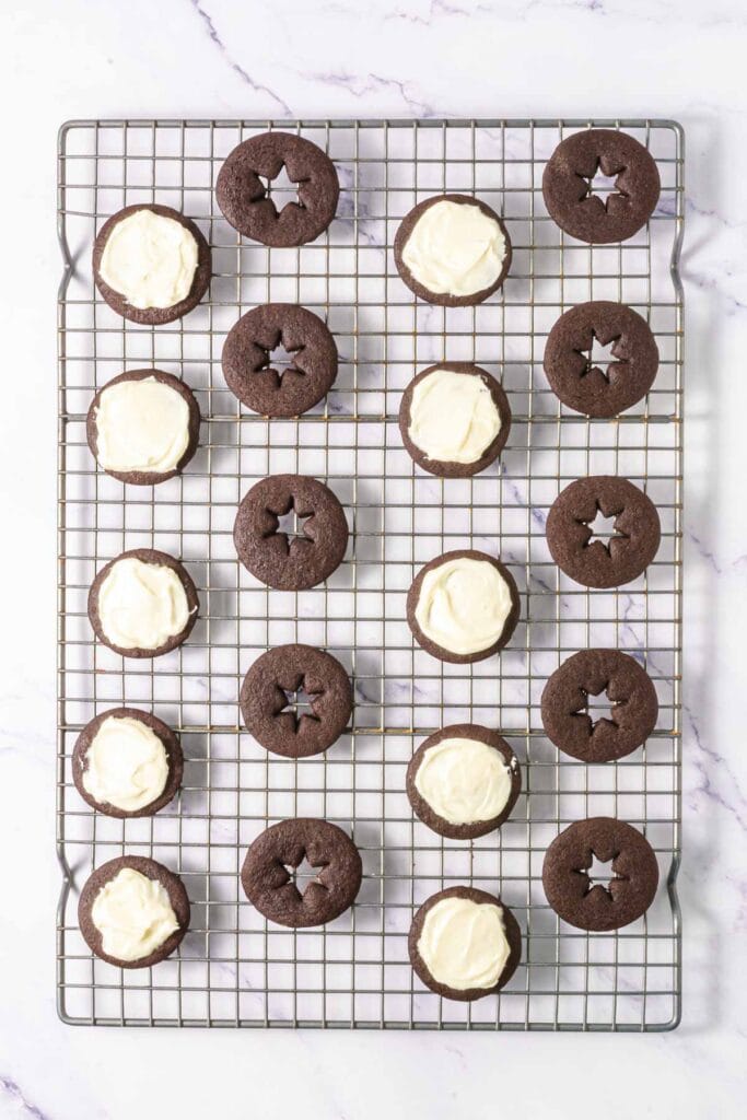 Chocolate Linzer Cookies with white icing and star-shaped cutouts cool on a rack, viewed from above&mdash;a delightful spin on the classic Linzer cookies recipe.
