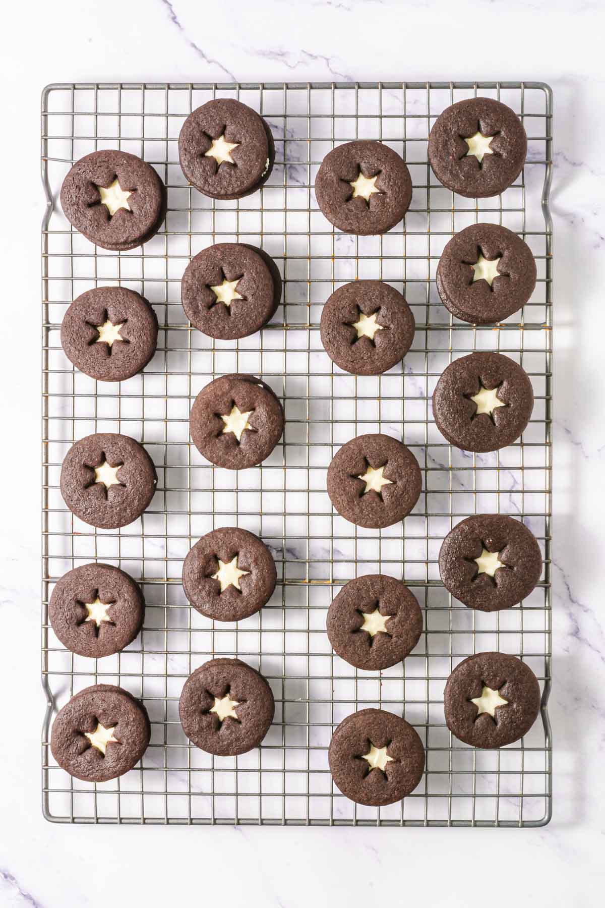 Chocolate Linzer Cookies with star-shaped cutouts rest on a cooling rack, seen from above&mdash;a delightful twist on the classic Linzer Cookies Recipe.