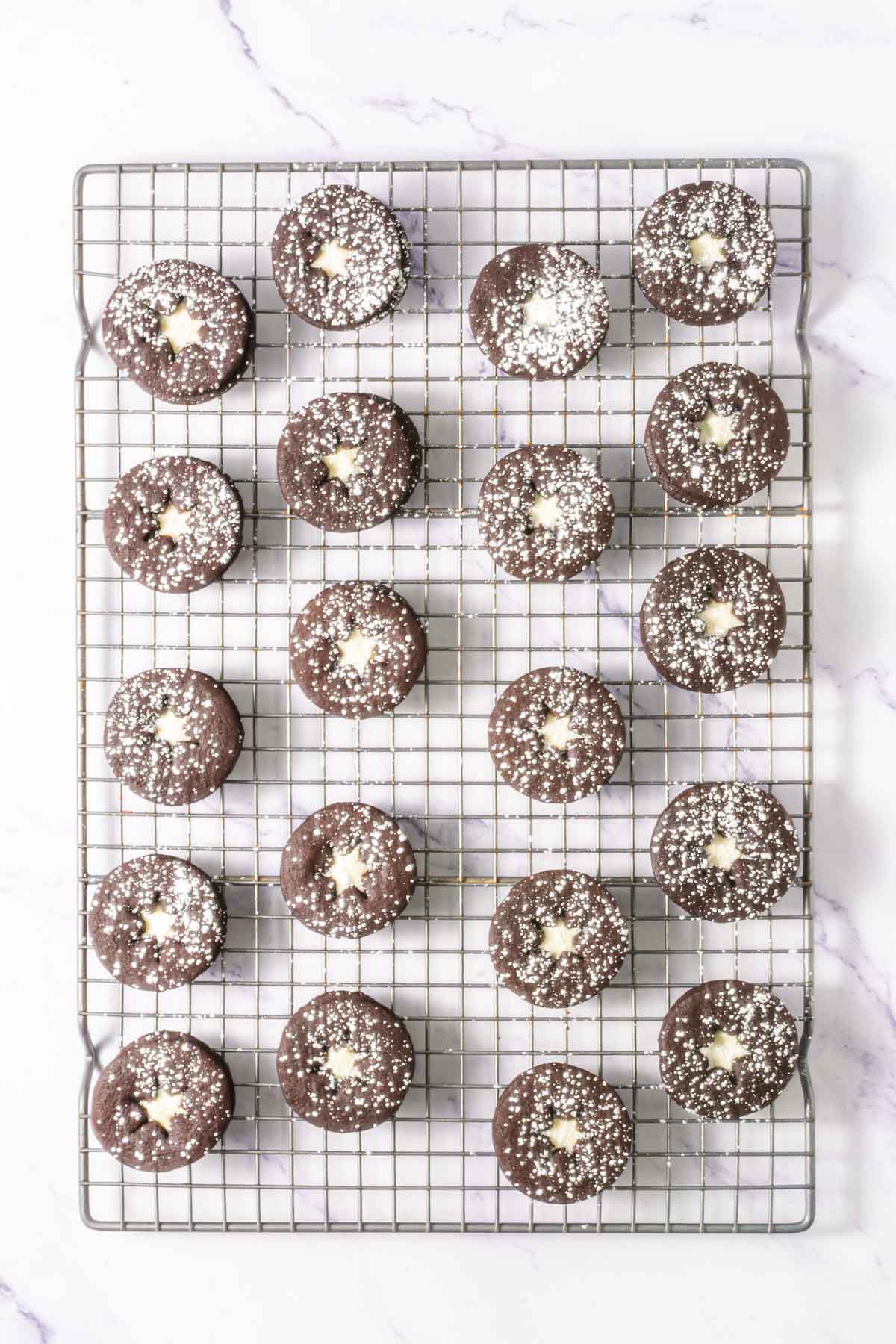Chocolate Linzer Cookies with powdered sugar and star-shaped centers rest on a cooling rack, viewed from above&mdash;a delightful twist on the classic Linzer Cookies recipe.