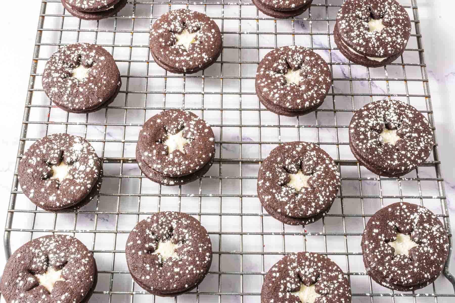 Chocolate Linzer Cookies with star-shaped cutouts and powdered sugar rest on a cooling rack&mdash;an irresistible twist on the classic Linzer Cookies Recipe.