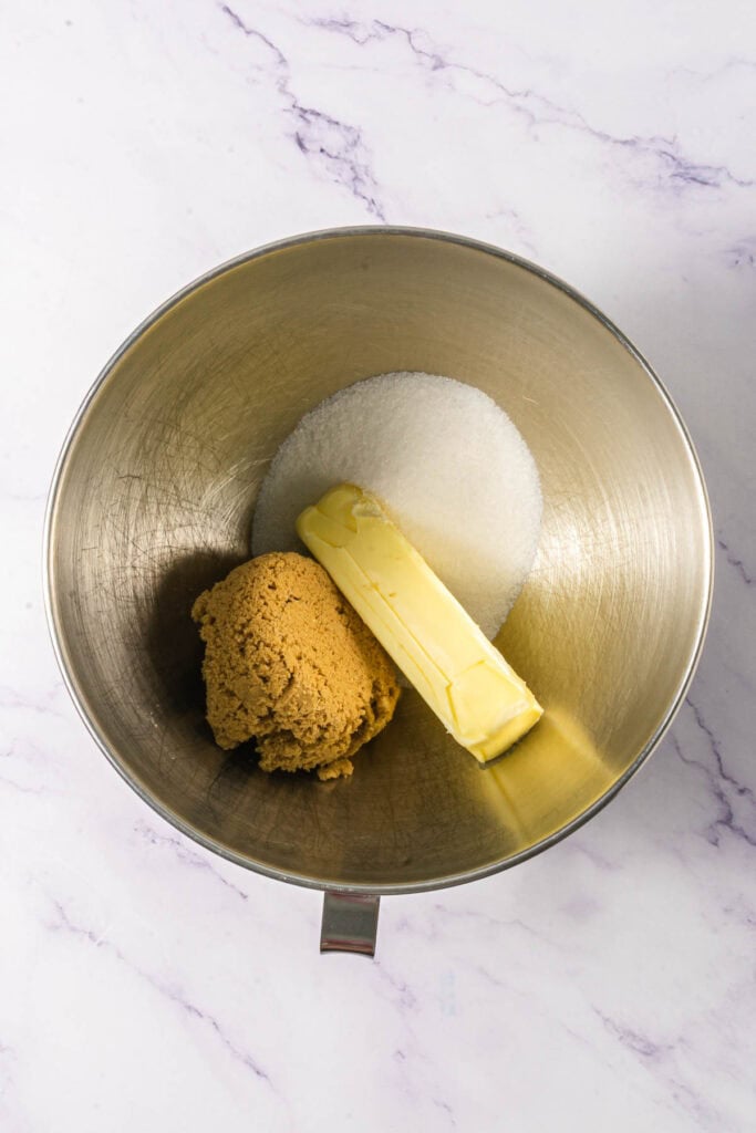 A mixing bowl with brown sugar, white sugar, and a stick of butter on a marble surface&mdash;perfect for starting your favorite Linzer Cookies Recipe.