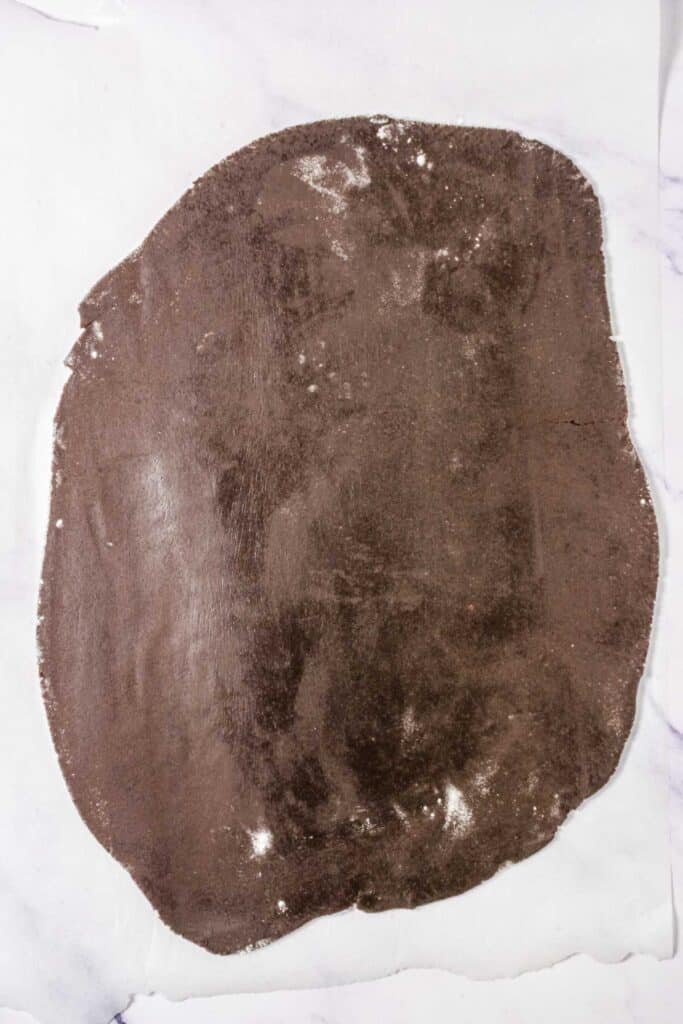 Rolled out sheet of chocolate dough on parchment paper, perfect for making Chocolate Linzer Cookies or classic Chocolate Cookies, ready to be cut or shaped.