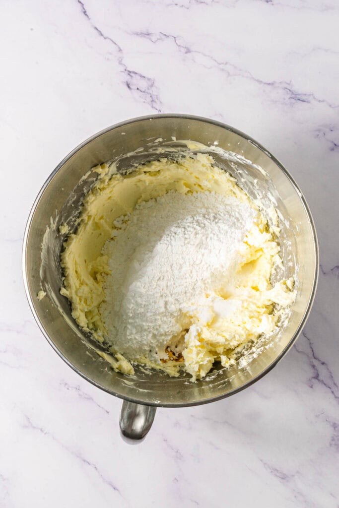 A metal mixing bowl with butter, sugar, and flour being combined on a marble countertop for delicious Linzer Cookies.