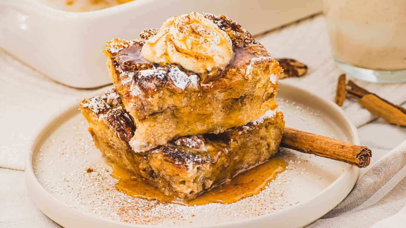 Two pieces of bread pudding topped with ice cream, cinnamon, and syrup on a plate with a cinnamon stick.