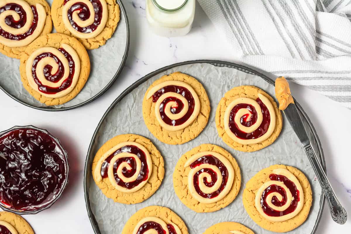 Crumbl copycat peanut butter and jelly cookies on plates, paired with a jar of milk and a bowl of jelly nearby.