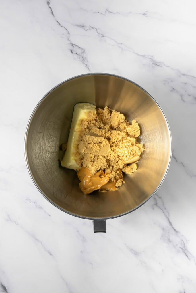 A mixing bowl with butter, brown sugar, and peanut butter on a white marble surface&mdash;perfect for making Crumbl copycat peanut butter and jelly cookies.