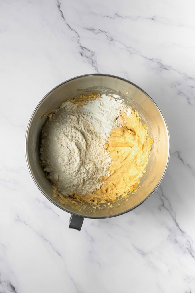 Metal mixing bowl with yellow batter and white flour on a marble surface, ready to whip up Crumbl copycat peanut butter and jelly cookies.