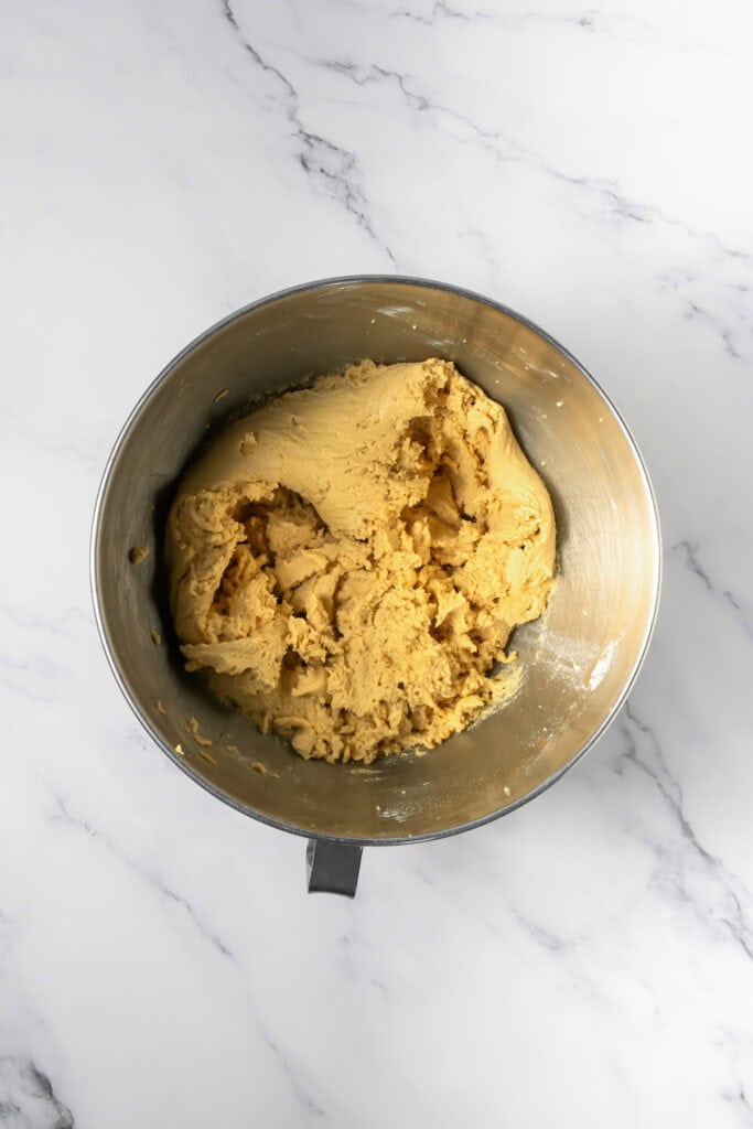 Metal mixing bowl filled with crumbl copycat peanut butter and jelly cookies dough on a white marble countertop.