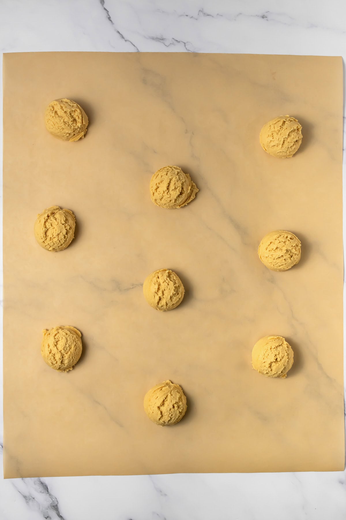 Nine scoops of crumbl copycat peanut butter and jelly cookie dough spaced out on parchment paper, ready for baking, on a marble surface.