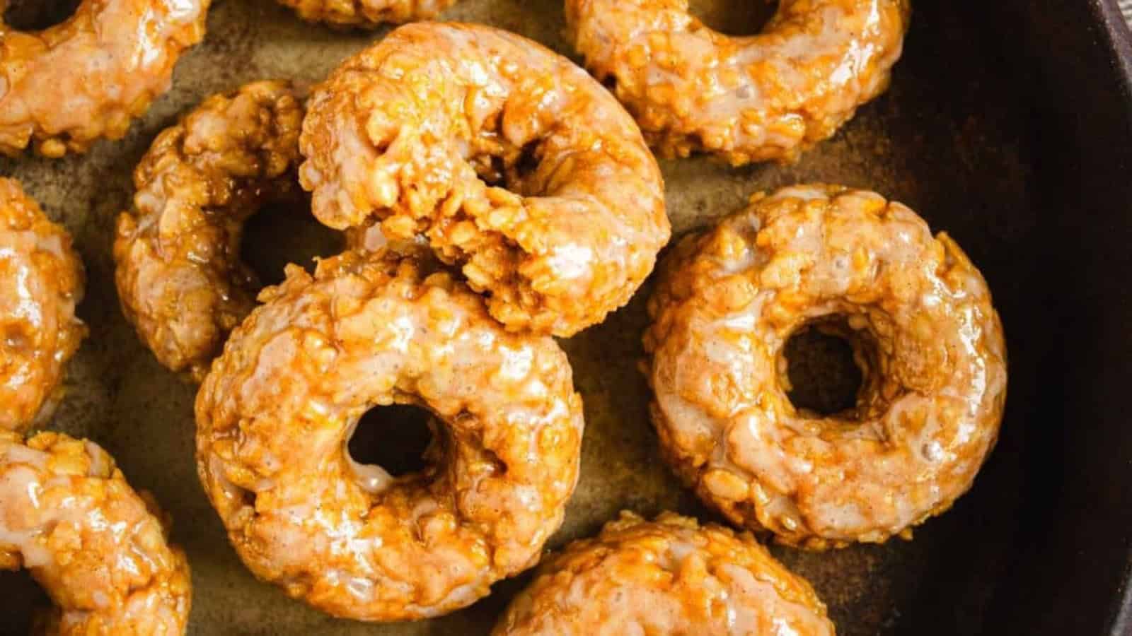 Glazed donuts with a crunchy texture arranged closely together on a dark baking sheet.