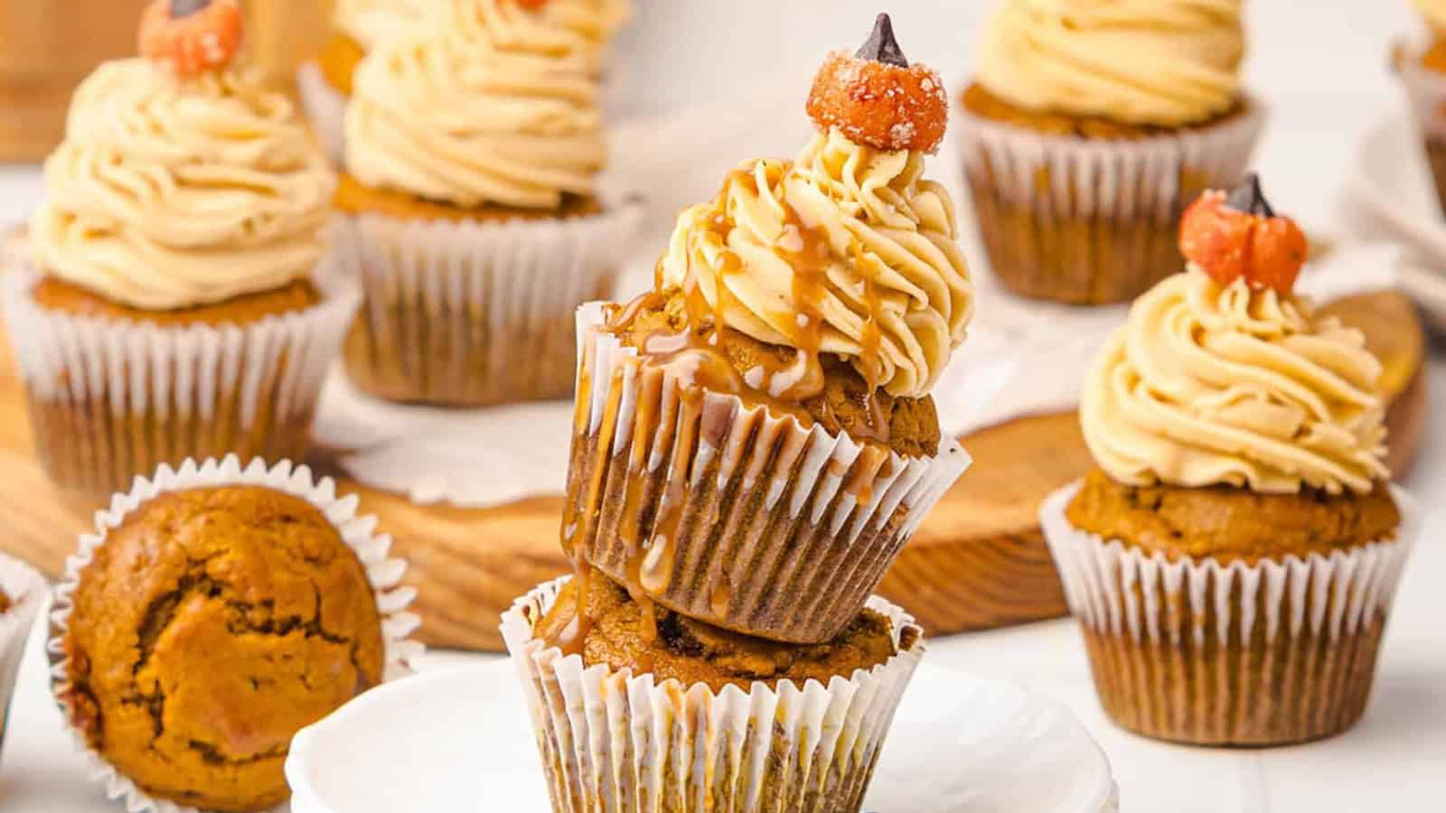 Pumpkin cupcakes with swirled frosting and caramel drizzle, topped with mini pumpkin decorations.